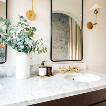 Close up image of vanity, brass sconces, black metal mirrors, and classic brass faucets.