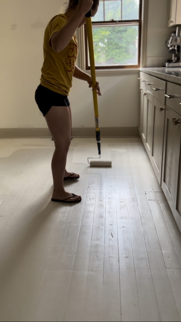 Katie putting a fresh base coat of paint on the floor before starting the design for the painted harlequin floor.