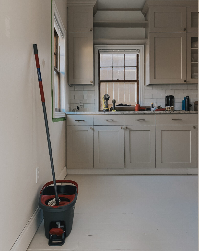 Mopping the floor to prep for paint. Image of a mop leaning against the wall of a kitchen.