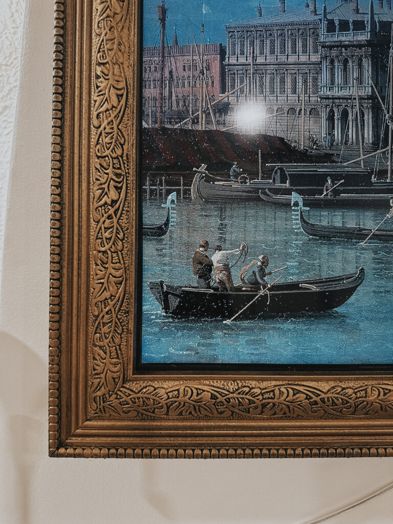 A close up image of a DIY tv frame. The art print displayed on the tv screen is a painting of people in boats coming to port in a city.