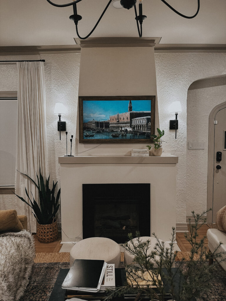 Image of a DIY tv frame hung horizontally on a mantel. A sconce sits on either side.