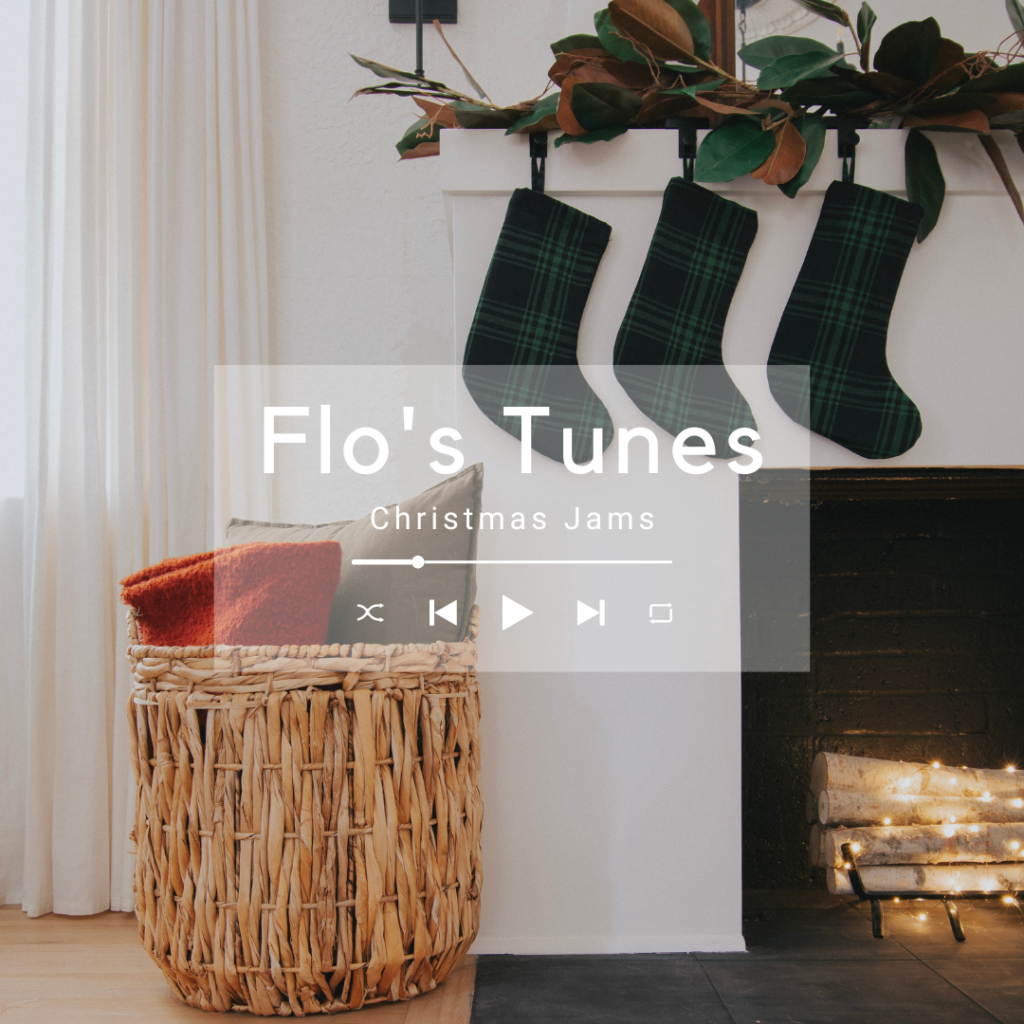 Image of fireplace with mantle set up for the holidays with a magnolia garland, green plaid stockings, and twinkle lights in the firebox.
A basket sits beside the fireplace with a pillow and blanket inside.

Text overlay says "Flo's Tunes, Christmas Jams".