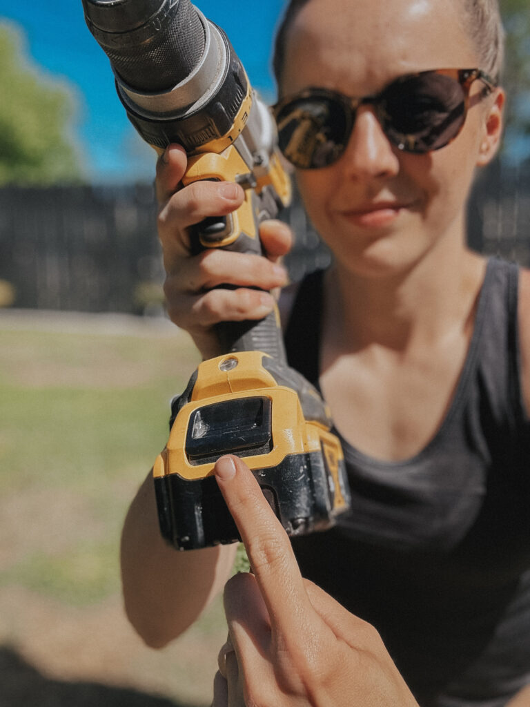 Holding a power drill and demonstrating the location of the battery release button.